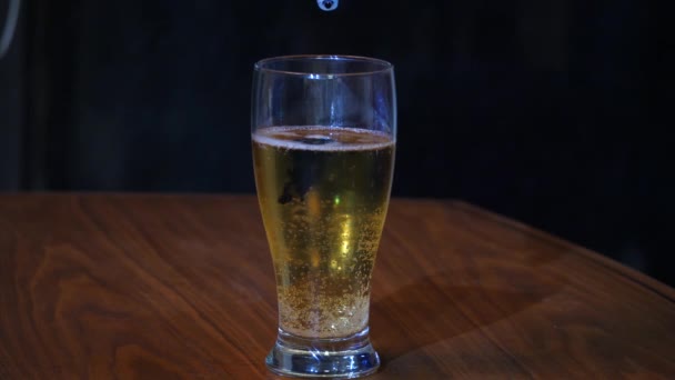 Vytvoření pivo sklo modré piva s pěnitou bílou hlavou pomocí potravinářské barvivo, oslavující sedí na tmavý dřevěný stůl, tmavě černé pozadí. — Stock video