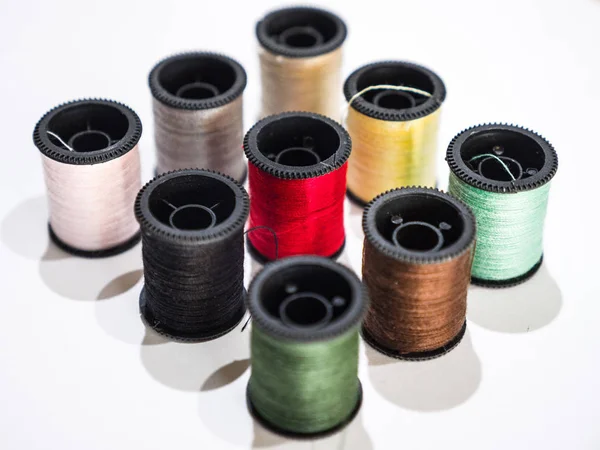 Closeup photograph of several rainbow colored spools of cotton thread or string including red, green, black, yellow, and white organized in rows and isolated on a white background.