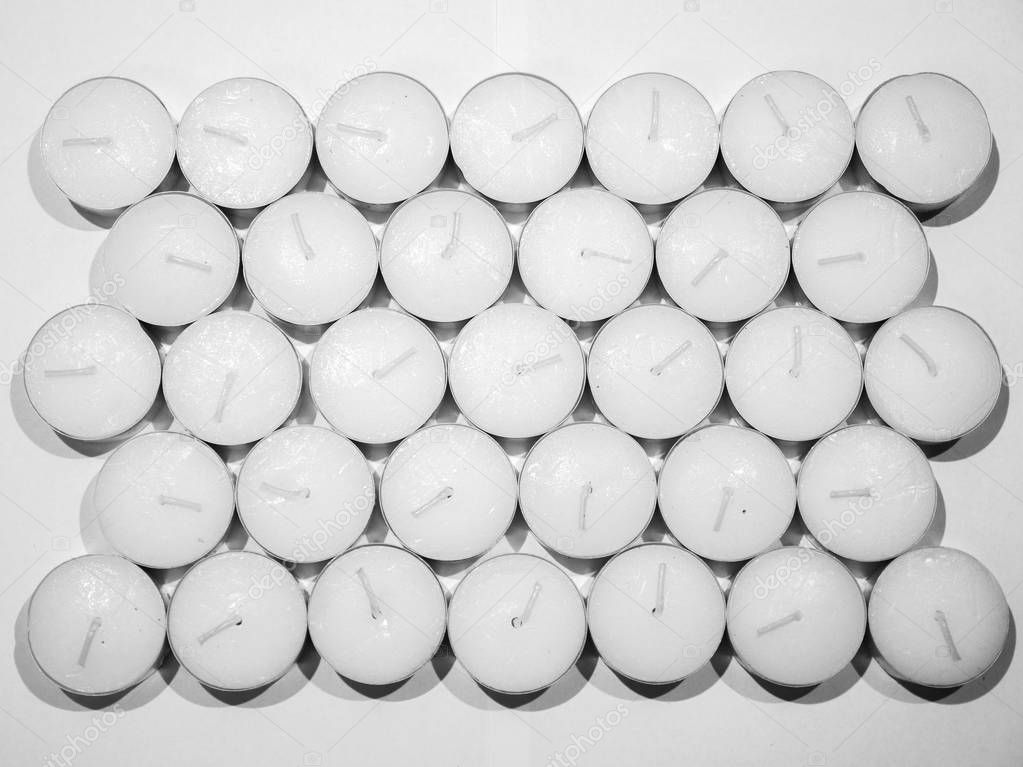 Closeup unsaturated photograph of lots of unlit white tea candles in silver colored metal enclosure organized in rows laid out on a counter making a beautiful background image, wallpaper or backdrop.
