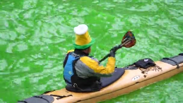 Chicago, Il - 17 maart-2018: Een feestelijk geklede man in een gele kajak boot maakt zijn weg naar beneden de helder groene vers geverfde Chicago River voor de jaarlijkse traditie van de St. Patrick's Day en viering. — Stockvideo