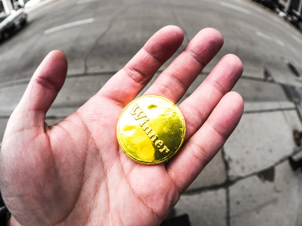 バック グラウンドでコンクリートの歩道に路上で手に金着色されたスズ箔エンボス幸運な勝者チョコレート コインを握って男の写真を閉じる — ストック写真