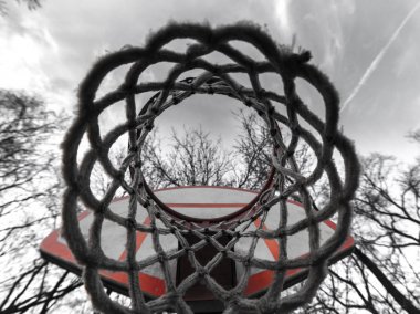 Bir şehir veya kent bahçesi basketbolda net ararken benzersiz fotoğraf görünümü kadar kapatın ve yukarıdaki gökyüzü, bulutlar ve ağaç dalları ve turuncu ve beyaz sedye ile delik.