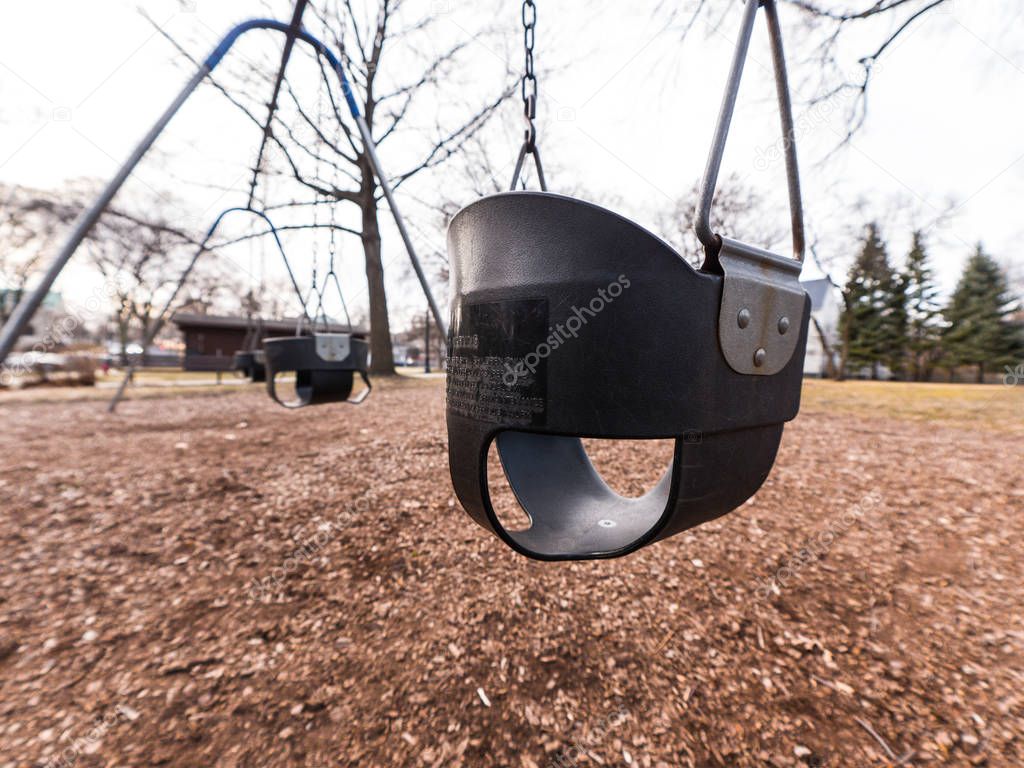 Close up photograph of a black rubber child's swing with weathered and rusted metal hooks and chains and brown dirt and wood chips below.