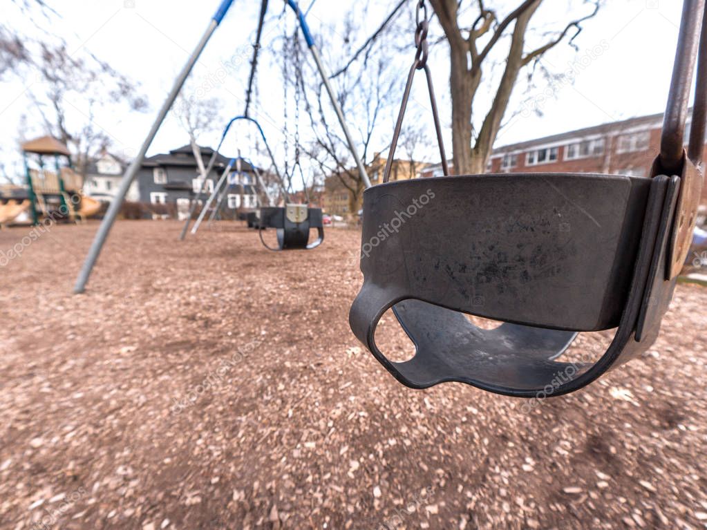 Close up photograph of a black rubber child's swing with weathered and rusted metal hooks and chains and brown dirt and wood chips below.