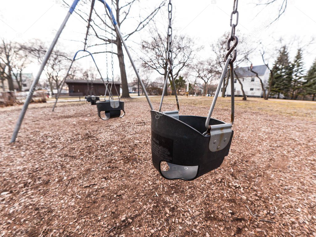 Close up photograph of a black rubber child's swing with weathered and rusted metal hooks and chains and brown dirt and wood chips below.