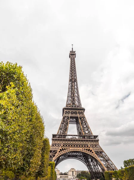 查看世界著名的埃菲尔铁塔纪念碑或地标与明亮的绿色树框架的看法和白色多云的天空超越在明亮的晴天在巴黎法国 — 图库照片