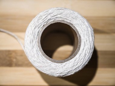 Bir karton tüp kenarında oturan ve bir Bambu tahta kesme kurulu arka plan üzerinde çözülüyor üzerinde ince beyaz dize bir beyaz örgülü rulo Close-Up yerleştirilmiştir.
