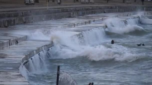Large waves crash and explode into the tiered concrete barriers and splash on the nearby walking surface near Foster Beach on a cold windy day in the Edgewater neighborhood in Chicago. — Stock Video