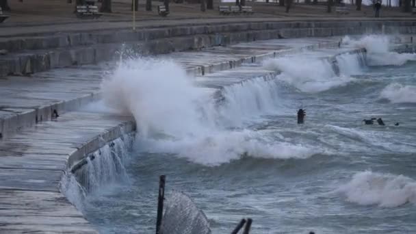 Slow Motion de grandes olas se estrella y explota en las barreras de hormigón estratificado y salpica en la superficie cercana a pie cerca de Foster Beach en un día frío y ventoso en el barrio Edgewater en Chicago . — Vídeo de stock