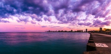 Chicago manzarası ile kabarık mor ve pembe bulutlar gökyüzünde yukarıda ve aşağıda mavi su Montrose Plajı'nda beton kıyı boyunca gün batımında güzel panorama fotoğrafı.
