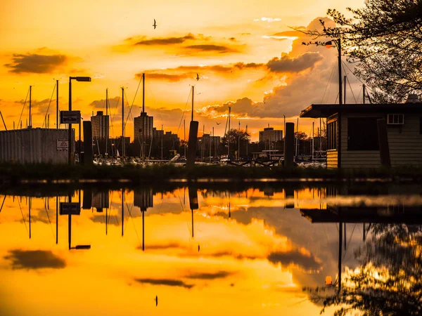 鮮やかなカラフルなオレンジと黄色の色のゴージャスな夕日空の上雲し ボートのモントローズ シカゴ港で水の反映 — ストック写真