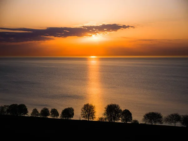 Beautiful sunrise over Lake Michigan in Chicago with calm water and orange and yellow colors reflecting from the sun and clouds above.