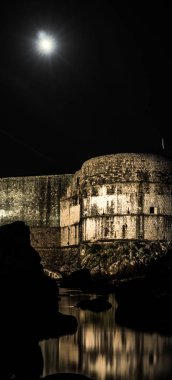 Güzel bir gece cityscape fotoğraf müstahkem duvar ve kayalık sahil Dubrovnik, Hırvatistan kentin su yansıtılmış yansıması ile aydınlandı aşağıdaki ve yukarıdaki ay.