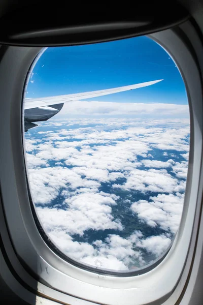 View looking out an airplane jet window on a calm sunny day with white clouds in a blue sky and land below making a beautiful travel background photograph image.
