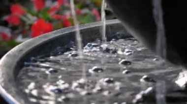 Havuza süzülen suyu yavaş çekimde kapat. Kabarcıklar oluştur ve arka planda kırmızı çiçekler olan siyah katmanlı granit bir çeşme ya da kase şeklinde bir çeşmeye su sıçrat..