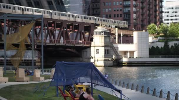 シカゴ イルー2019年7月13日 人々は街のリバーウォークに沿って配置された芸術を楽しみ Cta列車が頭上を通過するときにカラフルな芝生の椅子でリラックスします — ストック動画