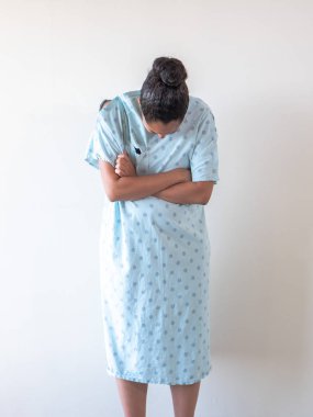 A young postpartum mixed race African American woman wearing a hospital gown or robe crosses her arms across her body as she hunches over crying tears of sadness or depression from a loss. clipart