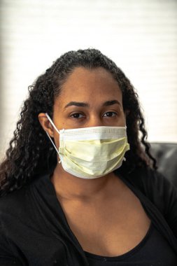 Caronavirus veya Covid-19 hastalığından korunmak umuduyla evindeki kanepede oturan güzel bir Afrikalı Amerikalı annenin yakın plan portresi..