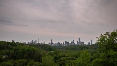 Toronto 'da gün batımında bulutlu, pembe ve mavi bir gökyüzü ve yakınlardaki ağaçlarla çevrili bir otoyolda trafik geçerken şehrin zaman çizelgesi yükseliyor..