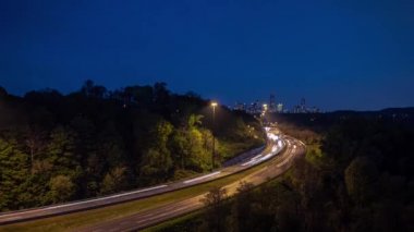 Gece vakti Toronto şehir merkezine uzanan kavisli otoyoldaki trafik ışıklarının ve stop lambalarının uzun süre açık kalması ve yolun kenarlarında ağaçların oluşturduğu gökyüzüne doğru uzanması..
