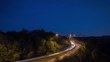 Dikey olarak gösterilen bir zaman çizelgesi uzun ışık yolları ve kavisli bir karayolu üzerindeki trafik geceleyin Toronto şehir merkezine doğru uzanan ağaçların yol kenarlarını kapladığı bir gökyüzü çizgisi..