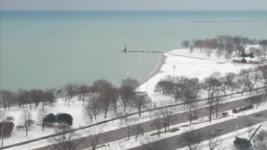 Chicago 'daki Lake Shore Drive' da araç trafiği ilerliyor. İnsanlar taze beyaz karda hareket ediyor. Michigan Gölü kıyıları boyunca açık alanlarda yüzeyi kaplıyorlar..