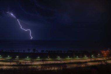Fırtına Michigan Gölü üzerinde ilerlerken ve arabalar gece vakti Chicago 'nun kuzey yakasındaki Lake Shore Drive' dan geçerken parlak bir şimşek çakıyor..