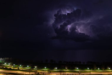 An intense thunderstorm cloud with blue or purple colors and lit up with numerous lightning strikes moves over Lake Michigan as cars pass by on Lake Shore Drive on Chicago's north side. clipart