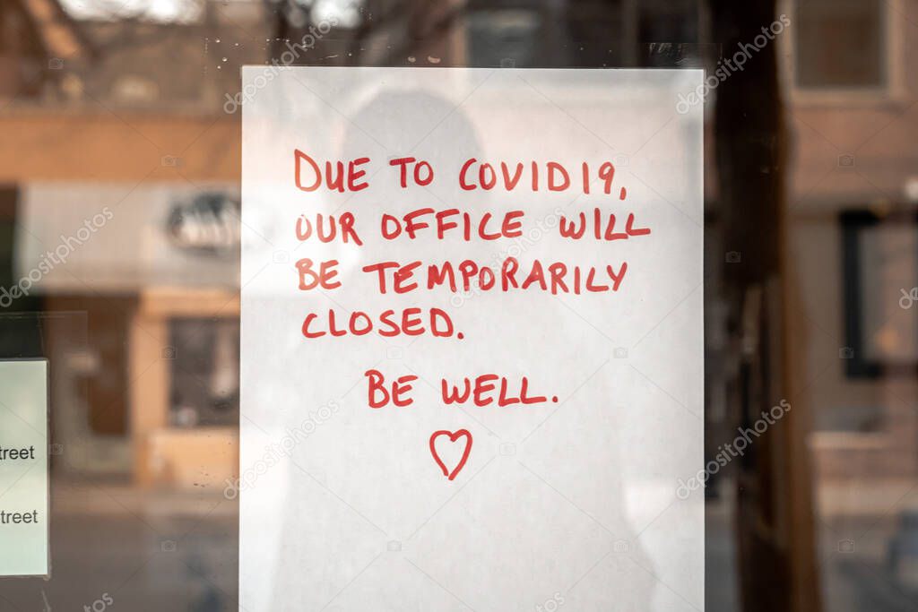 White piece of paper with red marker handwritten text and heart is taped to a glass storefront of a business or retail establishment in Chicago during the coronavirus pandemic and stay at home orders.