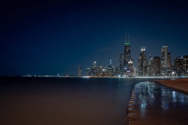 Chicago şehrinin gökyüzü gece fotoğrafı. Duran sudan yansıyan ışıklar Michigan Gölü boyunca uzanan beton kıyı şeridini silip süpürüyor..