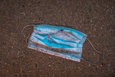 Kayıp, atılmış ya da düşmüş mavi, yıpranmış, kirli ve ıslak yüz maskesi, cerrahi doktor ya da lastik bantlı hemşire maskesi, Chicago şehir merkezinde kaldırım ya da beton kaldırımlar.