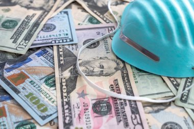 Tıbbi masraflar arka planında mavi solunum hastanesi doktor maskesi ya da yüzü tırtıklı doku ile kaplı bir yığın para ve COVID-19 geçmişi için yüz dolarlık banknotlar var..