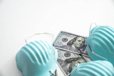 Solunum maskelerini örten üç mavi tıbbi yüzün COVID-19 koronavirüs salgını arkaplanı. Kaburgalar yüz dolarlık banknotlar seriyor. Beyaz arka planda izole edilmiş..