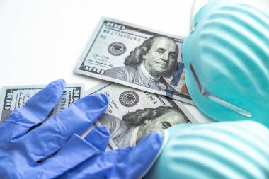Coronavirus COVID-19 salgınından korunmak için mavi kaburgalı tıbbi maskelerin ve kullanılmış lateks eldivenlerin altında yatan birkaç yüz dolarlık banknotlar veya nakit para..