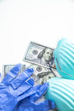 Coronavirus COVID-19 salgınından korunmak için mavi kaburgalı tıbbi maskelerin ve kullanılmış lateks eldivenlerin altında yatan birkaç yüz dolarlık banknotlar veya nakit para..