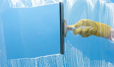 Mavi bir gökyüzü üstünde pencere temizleme sarı lastik eldiven el 