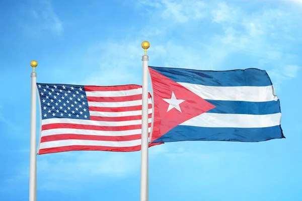 United States and Cuba two flags on flagpoles and blue cloudy sky background
