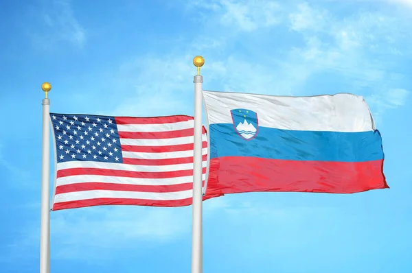 United States and Slovenia two flags on flagpoles and blue cloudy sky background