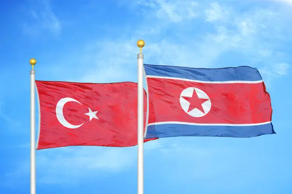 Turkey and North Korea two flags on flagpoles and blue cloudy sky background