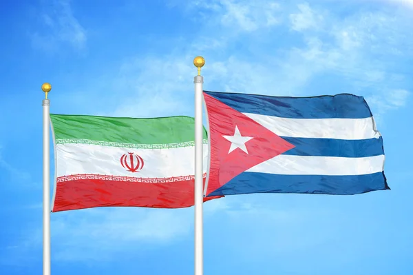 Iran and Cuba two flags on flagpoles and blue cloudy sky background