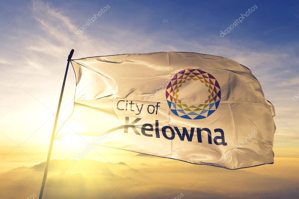 Kelowna of British Columbia of Canada flag textile cloth fabric waving on the top sunrise mist fog