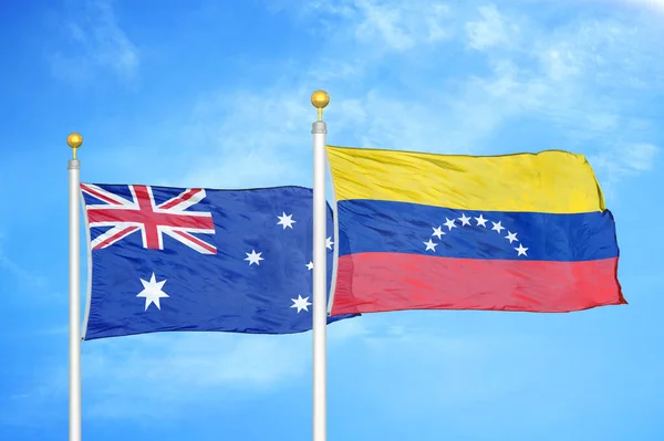 Australia and Venezuela two flags on flagpoles and blue cloudy sky background