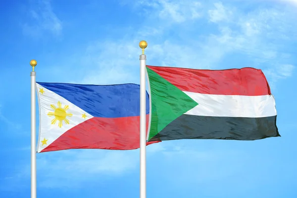 Philippines and Sudan two flags on flagpoles and blue cloudy sky background