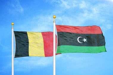Belçika ve Libya bayrak direkleri ve mavi bulutlu arka planda iki bayrak