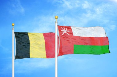 Belçika ve Umman bayrak direkleri ve mavi bulutlu arka planda iki bayrak