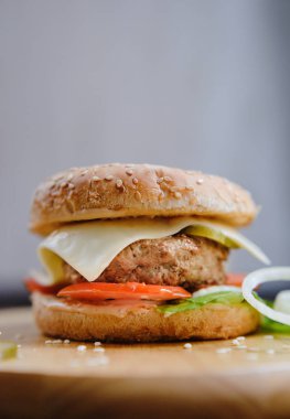 tavuk Patty, peynir, marul, domates, soğan ve turşu doğal ışık ahşap tepsi üzerinde yalan susam tohumu çörek üzerinde klasik Amerikan Burger