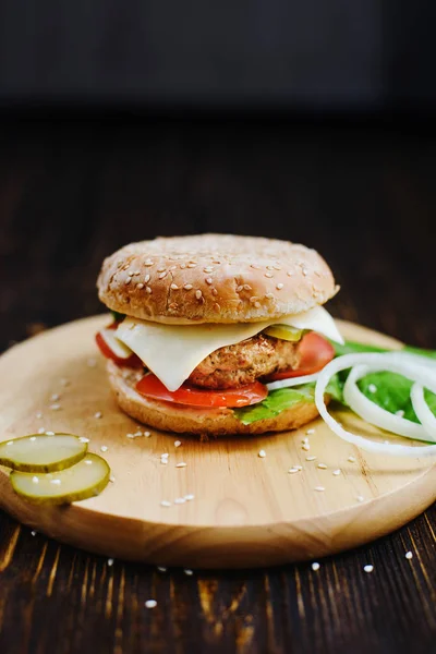 classic American Burger with chicken Patty, cheese, lettuce, tomatoes, onions and pickles on a sesame seed bun lying on the tray of natural light wood