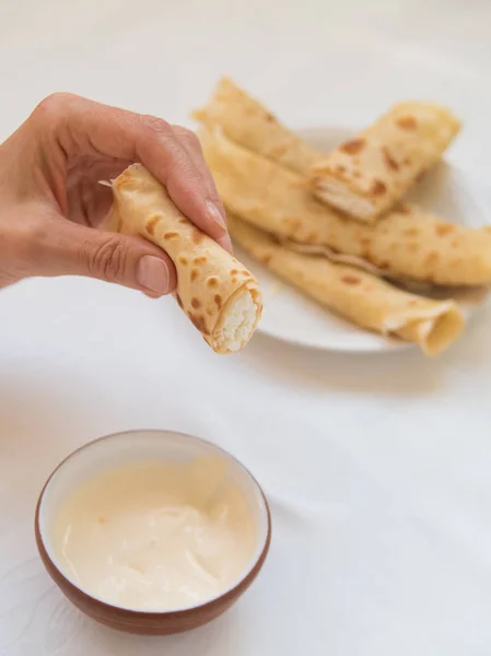 Vrouwelijke hand houden van de pancake roll onder plaat met zure room. — Stockfoto