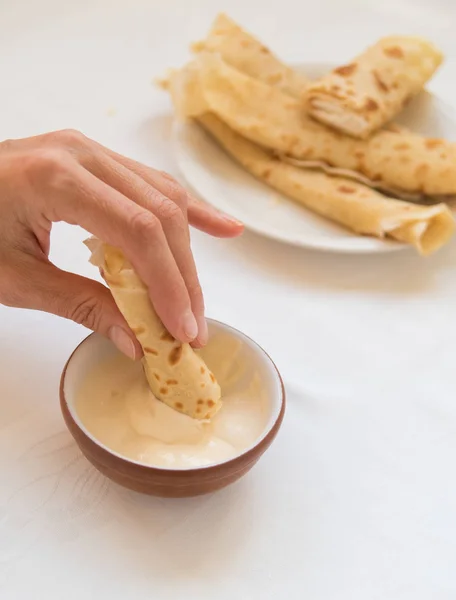 Vrouwelijke hand pancake roll dompelen in zure room. — Stockfoto