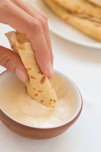 Vrouwelijke hand pancake roll dompelen in zure room. — Stockfoto